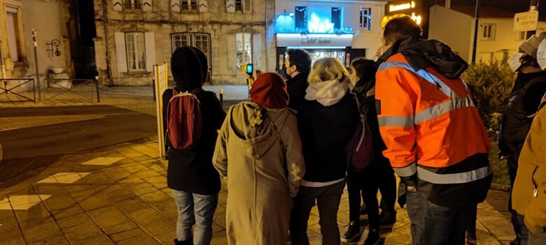 Un groupe de personnes de nuit dans une rue, participant à une balade thermo avec un conseiller caméra en main